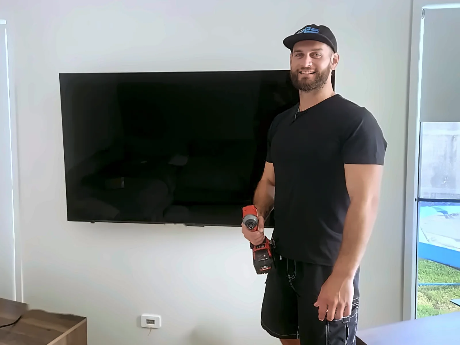 Josh from Mr Install standing beside a freshly wall-mounted TV, impact driver in hand